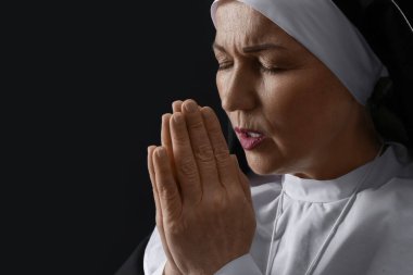 Olgun rahibe karanlık arka planda dua ediyor.