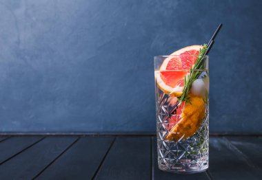 Bir bardak soğuk cin tonik ve koyu ahşap arka planda greyfurt dilimleri.