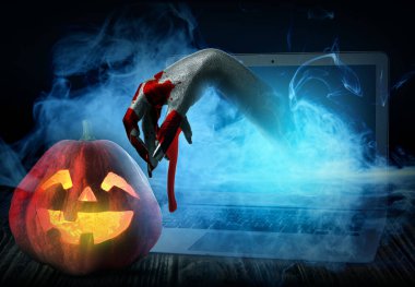 Cadılar Bayramı balkabağı ve cadı karanlık arka planda dizüstü bilgisayardan dışarı uzanıyor.