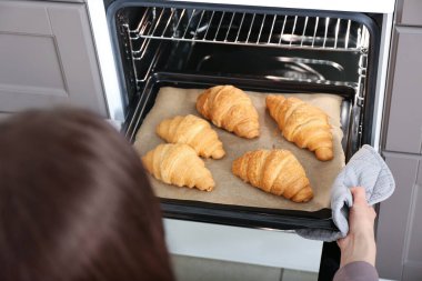 Fırından taze kruvasanla fırın tepsisi alan bir kadın.