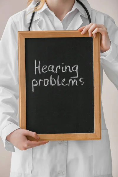 Female doctor holding board with text HEARING PROBLEMS on color background