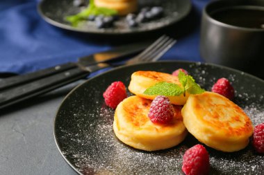 Koyu arkaplanda süzme peynirli krep ve ahududu tabağı, yakın plan.