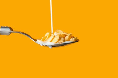 Renkli arka planda mısır gevrekleri olan kaşığa süt dökülüyor. Yakın plan.