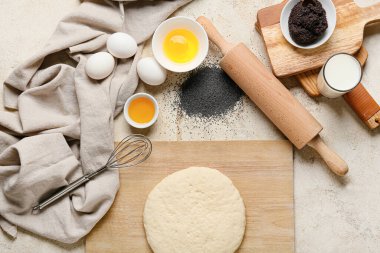 Haşhaş tohumu çöreği ve hafif arka planda malzemeler için taze hamurla ahşap tahta.