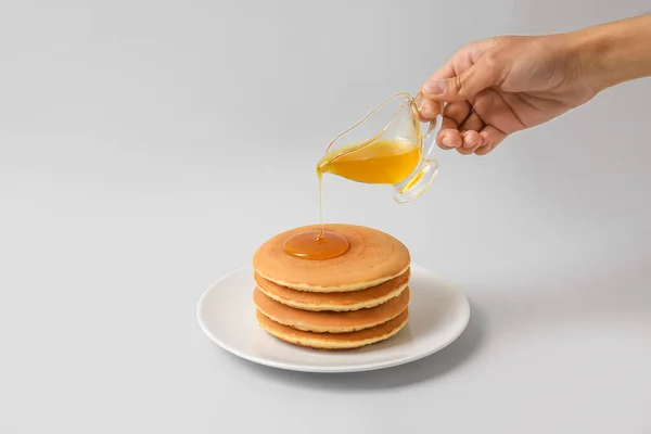 Wanita Menuangkan Madu Piring Dengan Pancake Lezat Latar Belakang Cahaya — Stok Foto