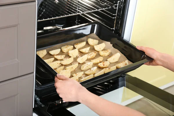 Woman putting tray with potato into oven