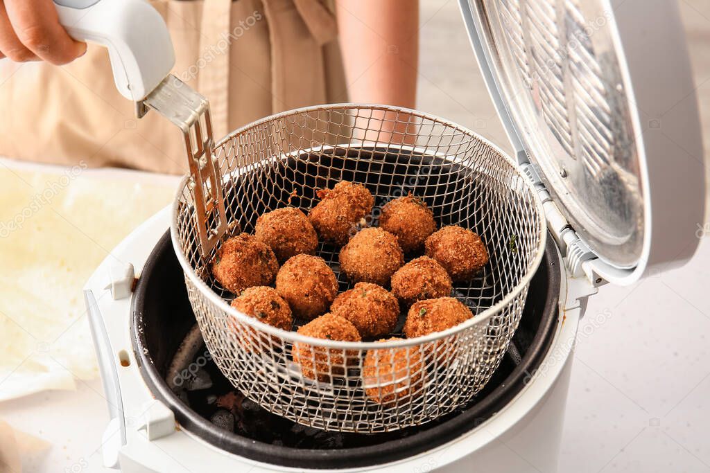 Woman holding basket with cod cutlets in deep fryer