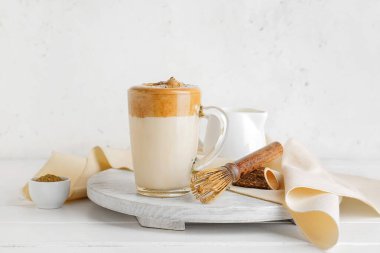 Bir bardak lezzetli dalgona hojicha latte ve açık arkaplanda chasen.