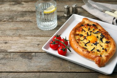 Lezzetli Ajarian Khachapuri tabağı ve ahşap arka planda bir bardak su.