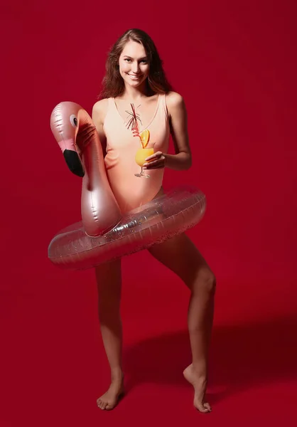 Young woman with cocktail and inflatable ring on color background