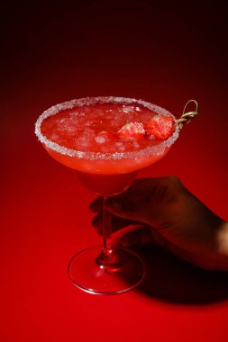 Renkli arkaplanda bir bardak lezzetli çilekli margarita tutan kadın.