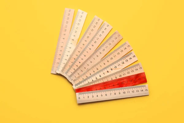 Red ruler among wooden ones on color background. Concept of uniqueness