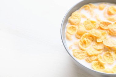 Hafif ahşap arka planda sütlü bir kase lezzetli mısır gevreği, yakın plan