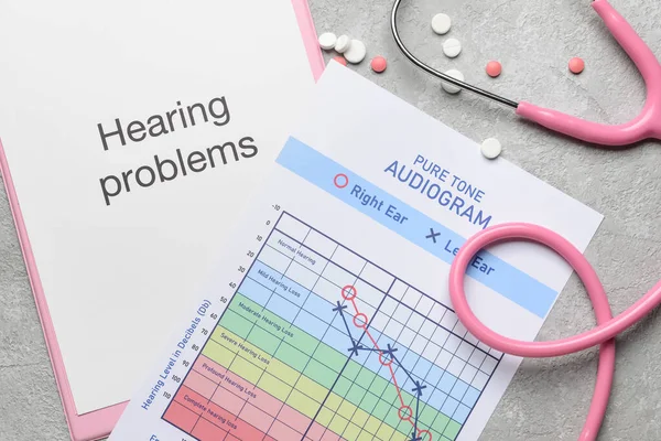 Clipboard with text HEARING PROBLEMS, stethoscope and audiogram on light background