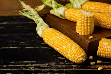 Koyu ahşap masada taze mısır koçanları, yakın plan.