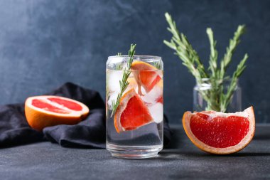 Bir bardak soğuk cin tonik ve arka planda greyfurt dilimleri.