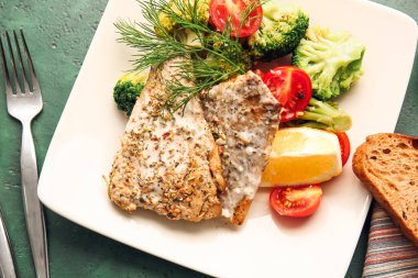 Renkli arka planda lezzetli morina filetosu ve sebzeli tabak, yakın plan.