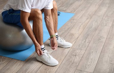 Spor salonunda ayakkabı bağcıklarını bağlayan genç bir adam.