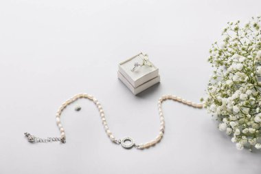 Nişan yüzüğü, kolye ve beyaz arka planda çingene çiçekleri olan bir kutu.