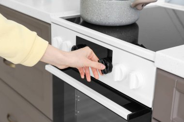 Kadın mutfakta elektrikli soba ayarlıyor.