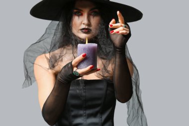 Gri arka planda mumu olan genç cadı.