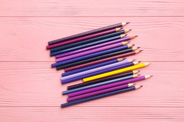 Yellow pencil among purple ones on color wooden background. Concept of uniqueness