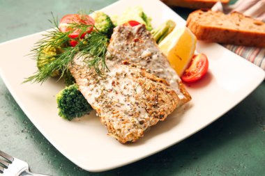 Renkli arka planda lezzetli morina filetosu ve sebzeli tabak, yakın plan.