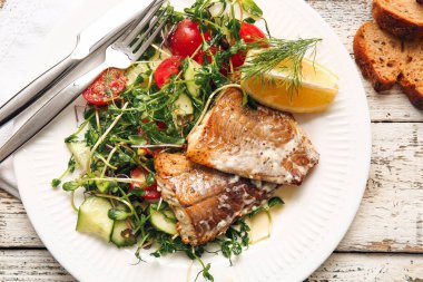 Lezzetli kızarmış morina filetosu ve hafif ahşap arka planda sebze tabağı.