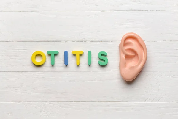 Word OTITIS and ear model on white wooden background