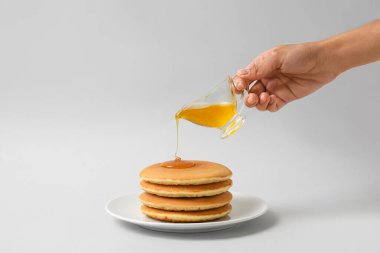 Kadın tabağa bal döküyor, arka planda leziz krepler var.