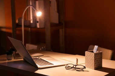 Karanlık odada modern laptop ve gözlüklerle rahat bir iş yeri.