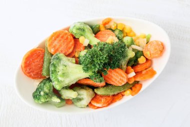 Arka planda farklı donmuş sebzelerle dolu bir kase.