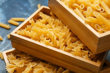 Renkli arka planda farklı türde pişmemiş makarna içeren ahşap kutular