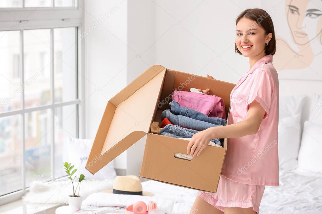 Young woman holding wardrobe box with clothes in bedroom