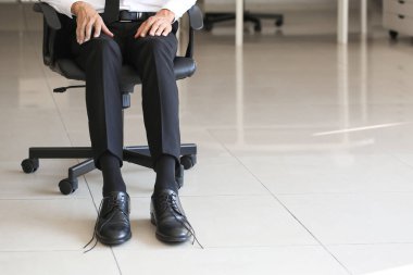 Ofiste sandalyede oturan bitmemiş ayakkabı bağcıkları olan bir iş adamı.