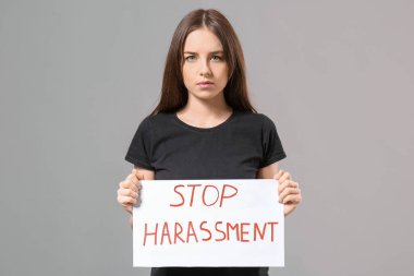 Elinde kağıt olan genç bir kadın gri arka planda DUR HARASSMENT