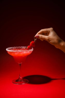 Renkli arkaplanda bir bardak lezzetli çilekli margarita ile kadın eli.