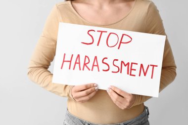 Elinde kağıt olan genç bir kadın gri arka planda DUR HARASSMENT
