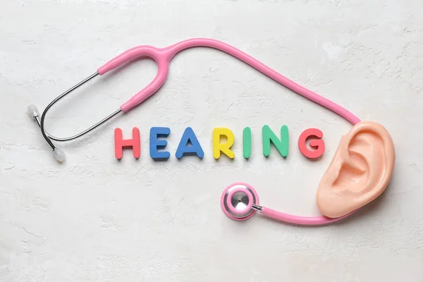 Word HEARING with stethoscope and ear model on white background