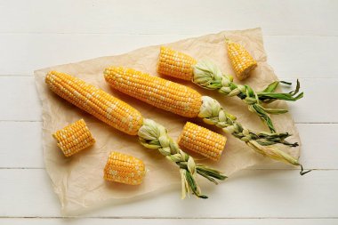 Beyaz ahşap masada taze mısır koçanları ve parşömen.