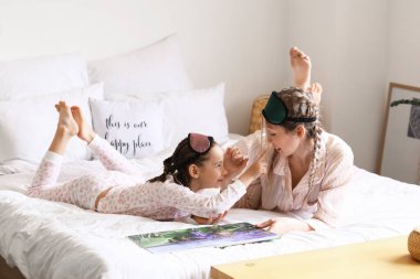 Küçük kız ve annesi yatak odasında masal okuyorlar.