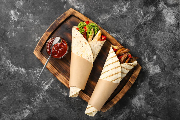 Wooden board with tasty Fajitas and sauce on dark background