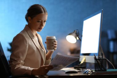 Gece geç saatlerde ofiste çalışırken kahve içen genç bir kadın.