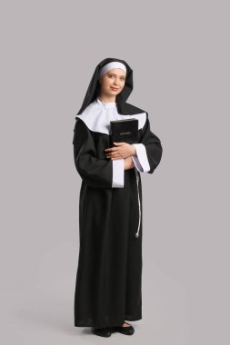 Gri arka planda İncil 'i olan genç rahibe.