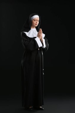 Karanlık arka planda dua eden genç rahibe.