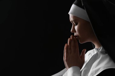 Karanlık arka planda dua eden genç rahibe.