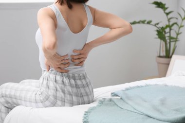 Yatak odasında sırt ağrısı çeken genç bir kadın.