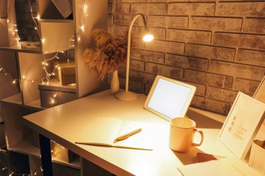 Duvarın yanında parlayan lamba, ışıklar ve tablet bilgisayarı olan modern iş yeri
