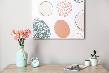 İçinde güzel karanfiller, ev bitkileri, saat ve dergi olan vazolar masada.