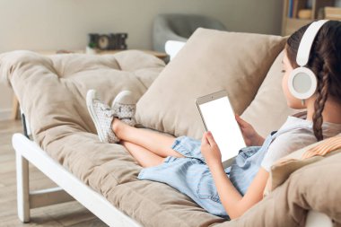 Tabletli küçük kız evde sesli kitap dinliyor.